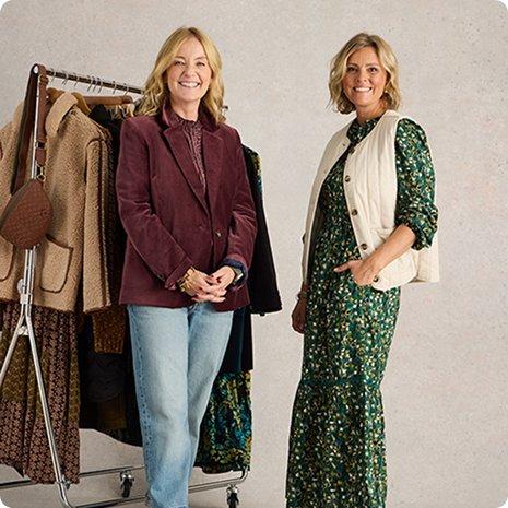 two women standing next to each other in front of a rack of clothes